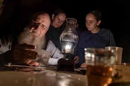 Henrique Loewen, with his daughters, looks at a photo of his old friend, Isaac Peter, by candlelight; Peter has a fatal melanoma.